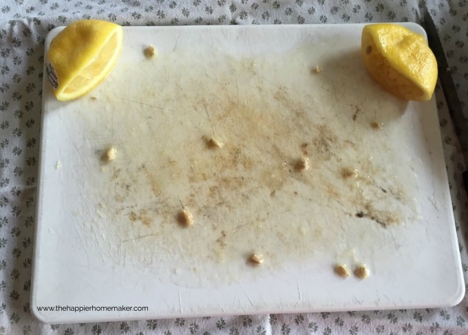 A close up of a dirty plastic cutting board with a cut lemon and lemon juice over the board