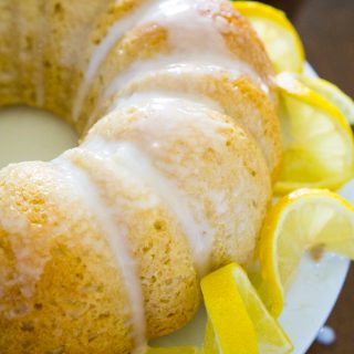 A close up of a limoncello bundt cake on a white cake stand with lemon garnish