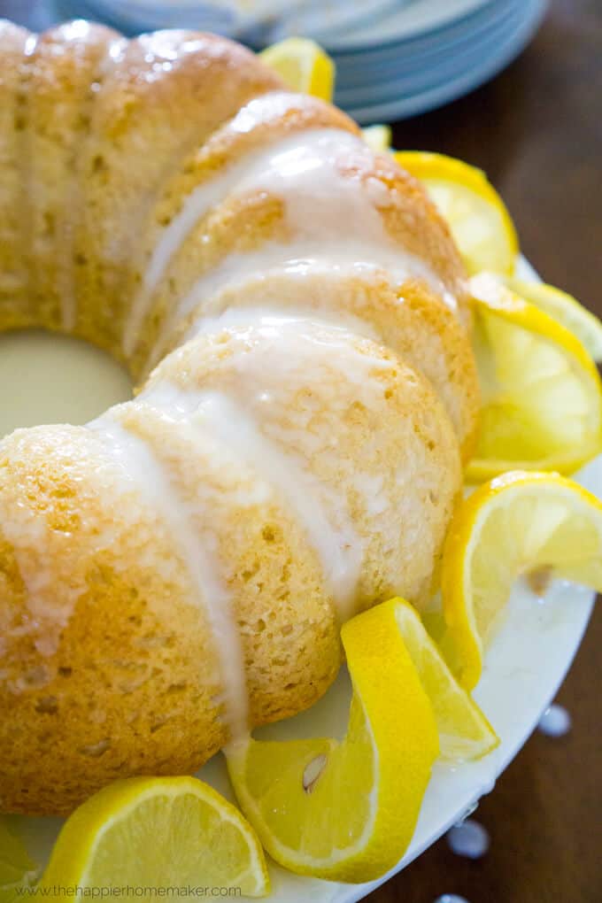 A close up of a limoncello bundt cake on a white cake stand with lemon garnish