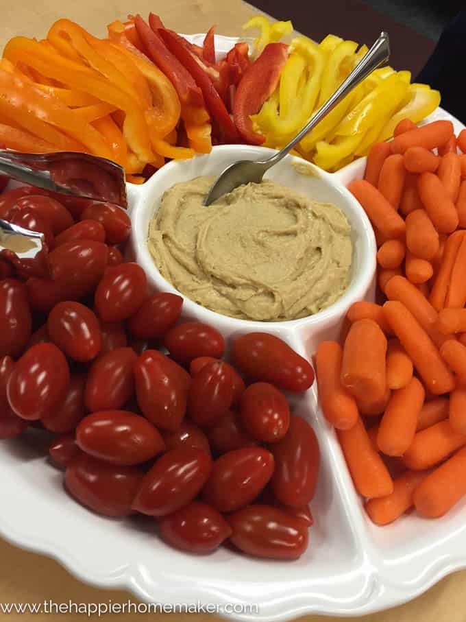 A close up of finger food snacks including carrots, peppers, cherry tomatoes and hummus 