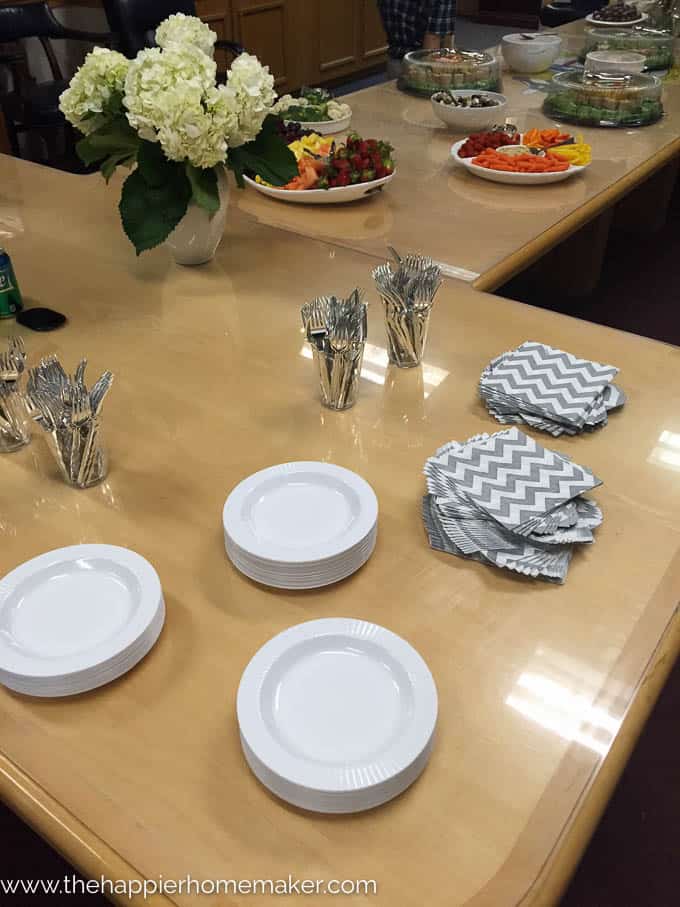 A table prepared for a party with silverware, plates, flowers and snacks