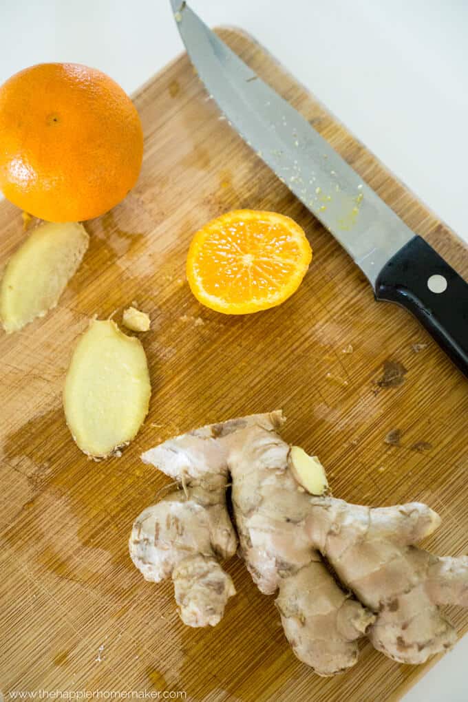 A cutting board with a knife, sliced oranges and ginger root