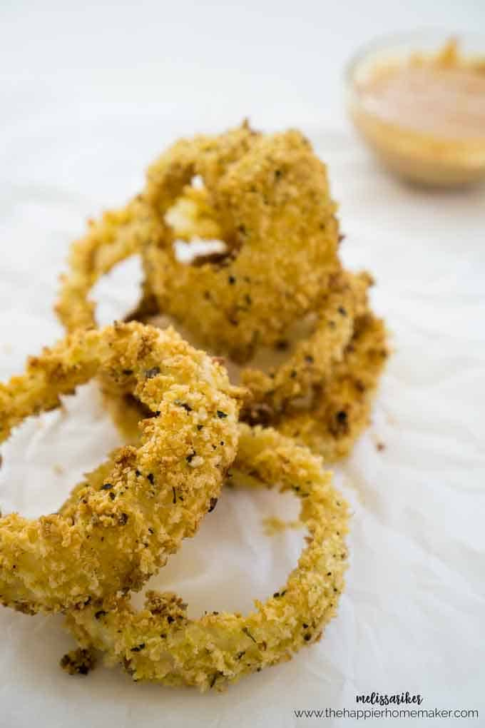 A close up of baked onion rings stacked on parchment paper