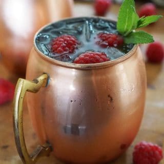 A close up of raspberry Moscow mule topped with raspberries and mint