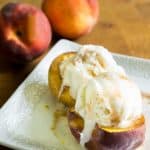 Baked peaches with brown sugar and cinnamon topped with ice cream on a small white platter
