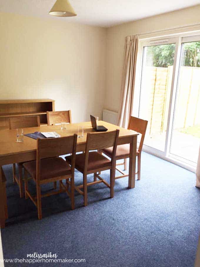 A plain dining room with a table and shelf in the background