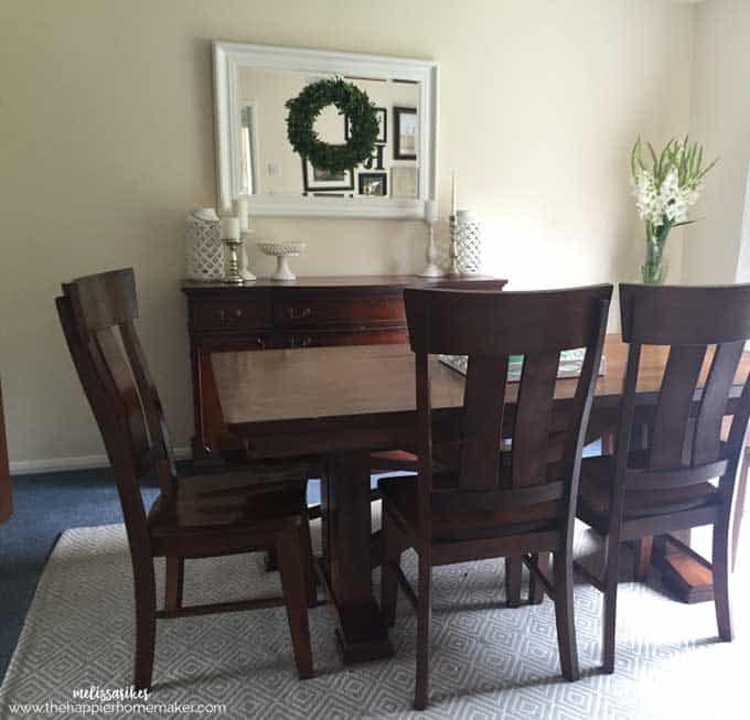 A brown dining room table with mirror and wreath in the background