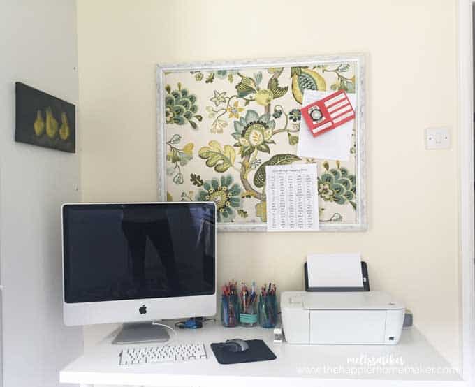 A desktop computer sitting on top of a desk with a printer next to it and a decorative pin board on the wall