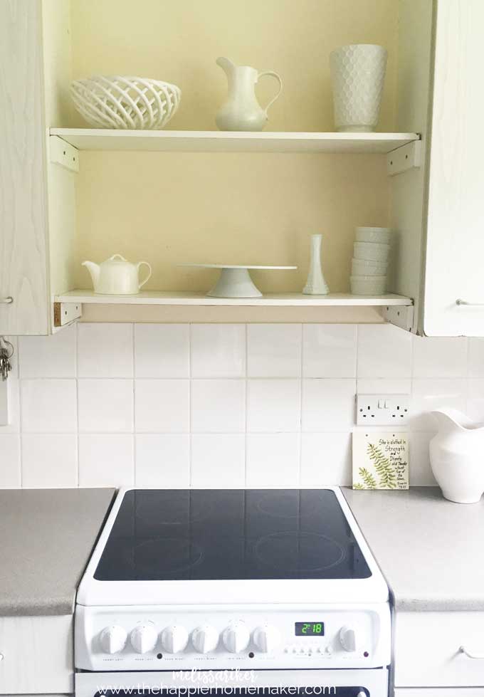A picture of an electric cooktop with two shelves above it with various white bowls, vases and kitchen ware