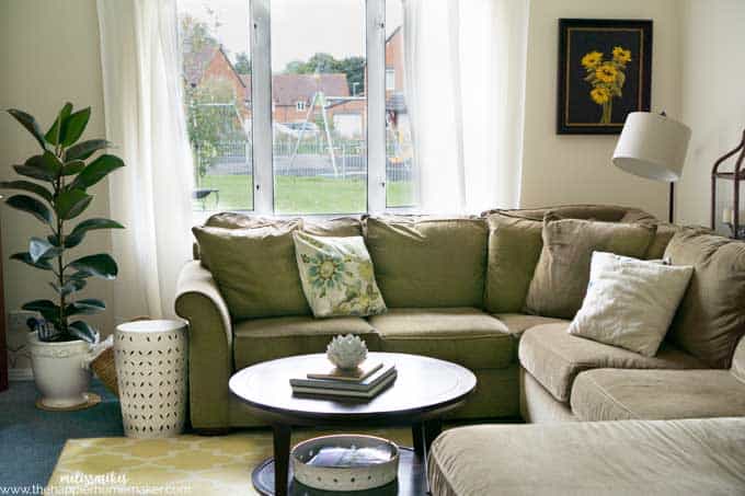 A living room with large green sofa, dark wood coffee table and white side table