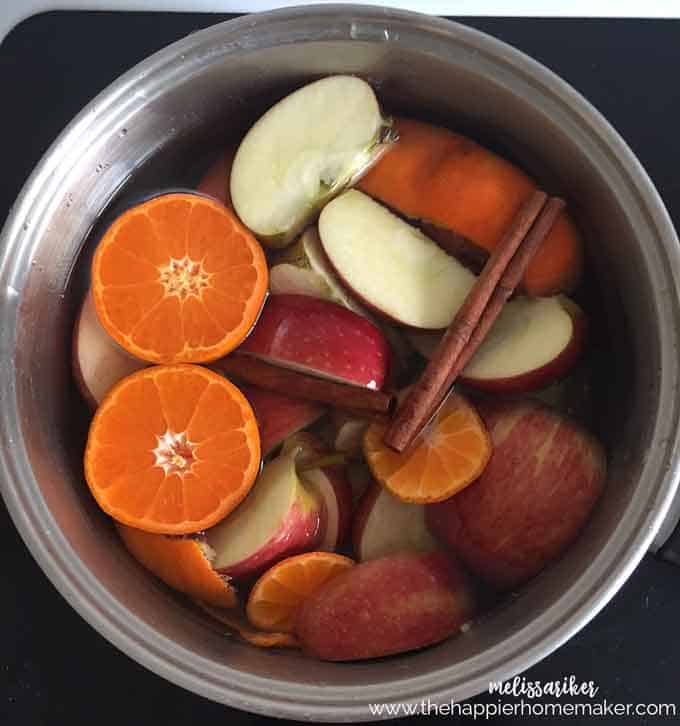 pot filled with halved oranges, sliced apples and cinnamon