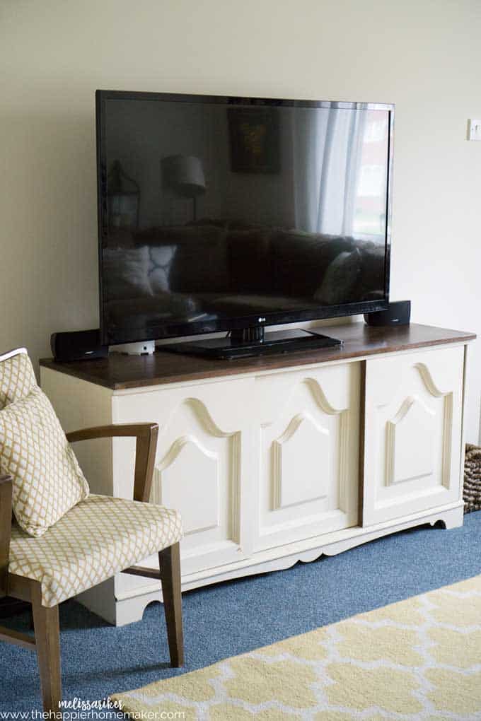 A tv sitting on a white bureau next to a chair 