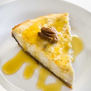 A slice of maple vanilla cheesecake on a white plate with syrup and pecan