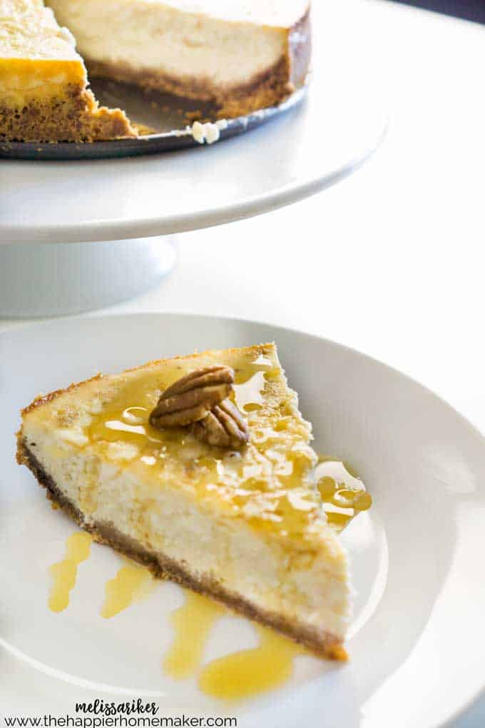 A slice of maple vanilla cheesecake on a white plate with syrup and pecan