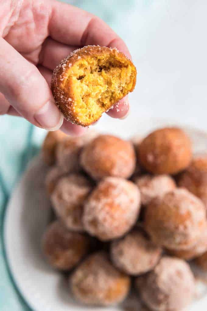 pumpkin doughnut holes on white plate with hand holding one