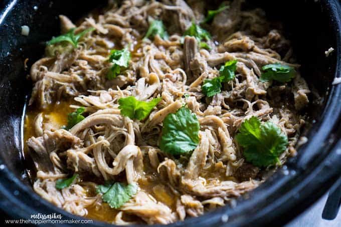 A slow cooker filled with Pork Carnitas garnished with parsley 