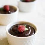 Three bowls of chocolate mousse topped with a fresh raspberry