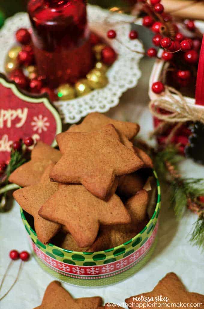 Homemade gingerbread cookies in a tin surrounded by Christmas decorations 