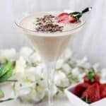 A chocolate martini garnished with fresh strawberries and shaved chocolate in front of white flowers and strawberries