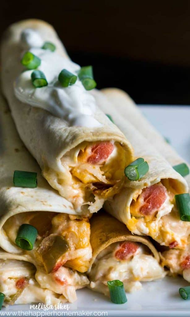 A close up of chicken taquitos garnished with green onions and sour cream
