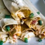 A close up of creamy cheesy chicken taquitos garnished with green onions