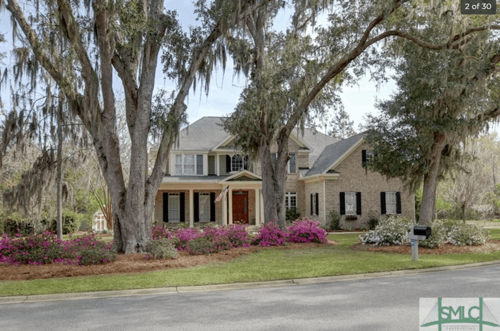 Two live oaks with Spanish moss in front of brick home with black shutters