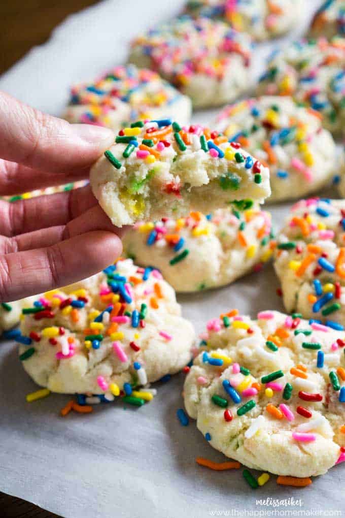 hand holding half of a funfetti cookie with more cookies in the background on parchment paper