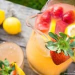 A close up of a pitcher of strawberry lemonade with fresh strawberries and slices of lemons