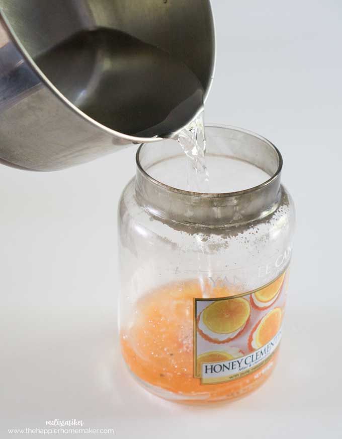 A close up of pouring water into the bottom of a mostly used glass candle