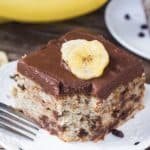 A piece of chocolate chip banana cake with chocolate frosting and slices of fresh banana on top. 
