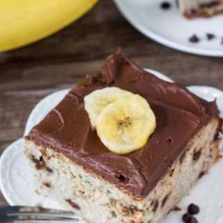 A piece of chocolate chip banana cake with chocolate frosting and slices of fresh banana on top.