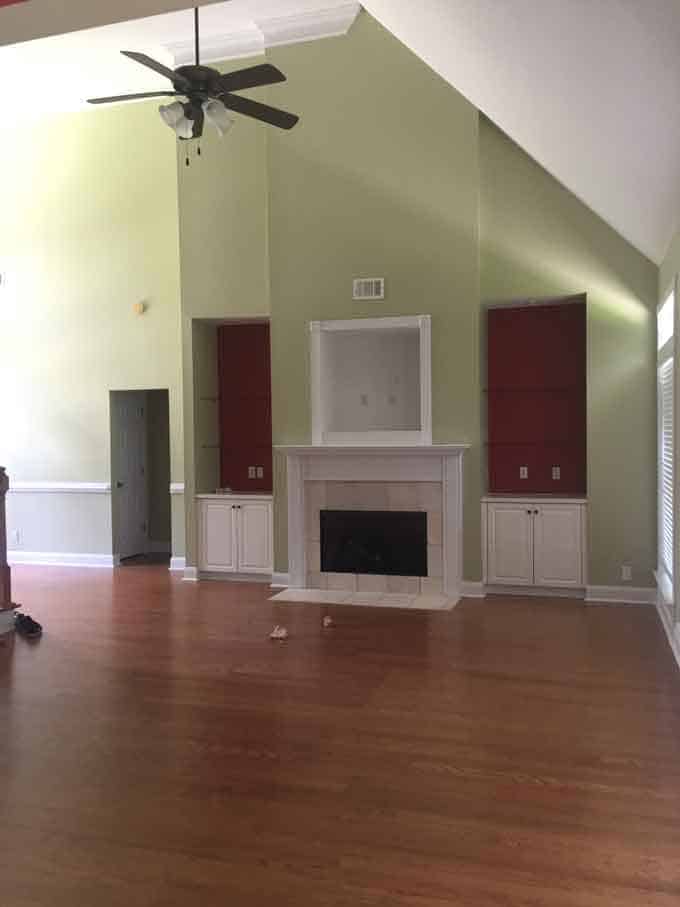 A large empty room with a wood floor and dated green and maroon walls