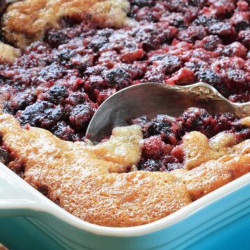mixed berry cobbler in a blue baking dish with silver spoon