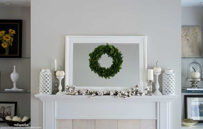 A close up of a white mantel with mirror and green wreath
