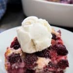 A close up of a slice of berry cobbler on a white plate topped with scoop of vanilla ice cream