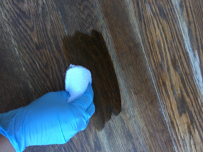gloved hand wiping wood with stain