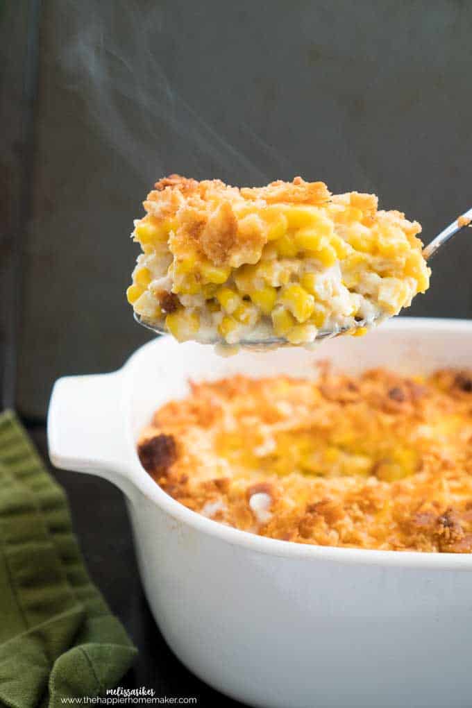 A close up or a spoon full of traditional corn pudding in a white baking dish