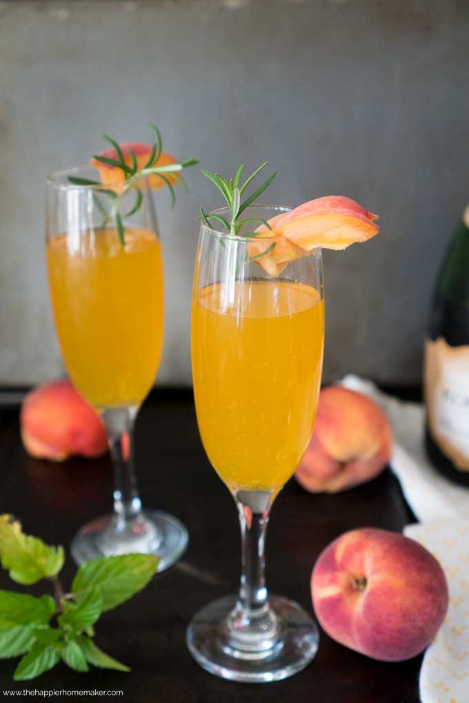 Two Bellini and Champagne cocktails garnished with a peach and rosemary