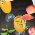 A Bellini and Champagne cocktail garnished with a peach and rosemary