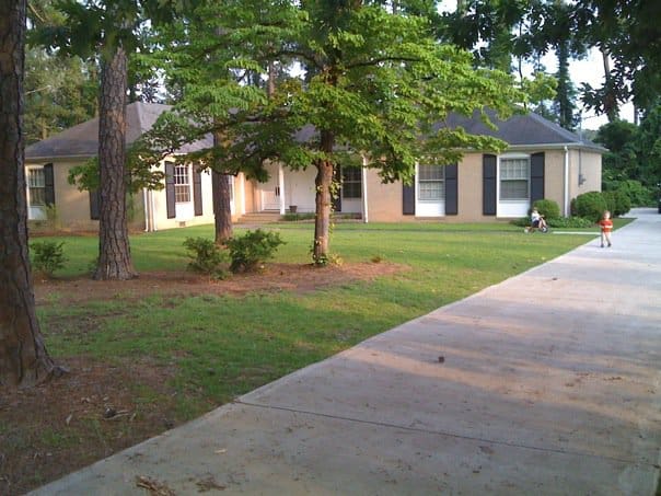 one story home with trees in front and long driveway