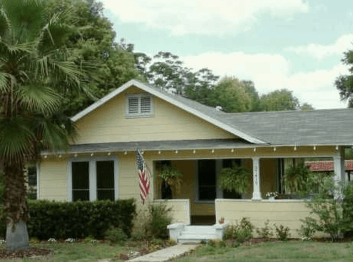 yellow bungalow with American flag and ferns hanging on porch