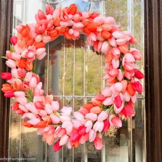 A close up of a pink tulip wreath hanging on a glass pane in a wooden door