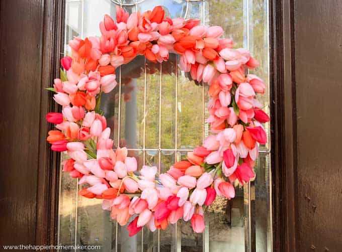 A close up of a pink tulip wreath hanging on a glass pane in a wooden door