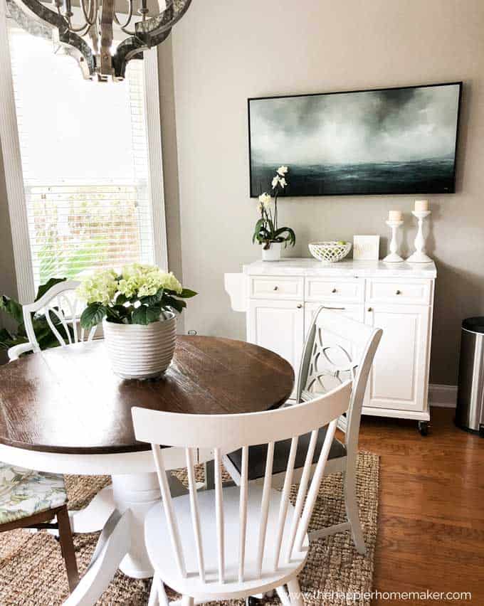 eat in kitchen with round table and chairs with white rolling kitchen island and ocean painting in background