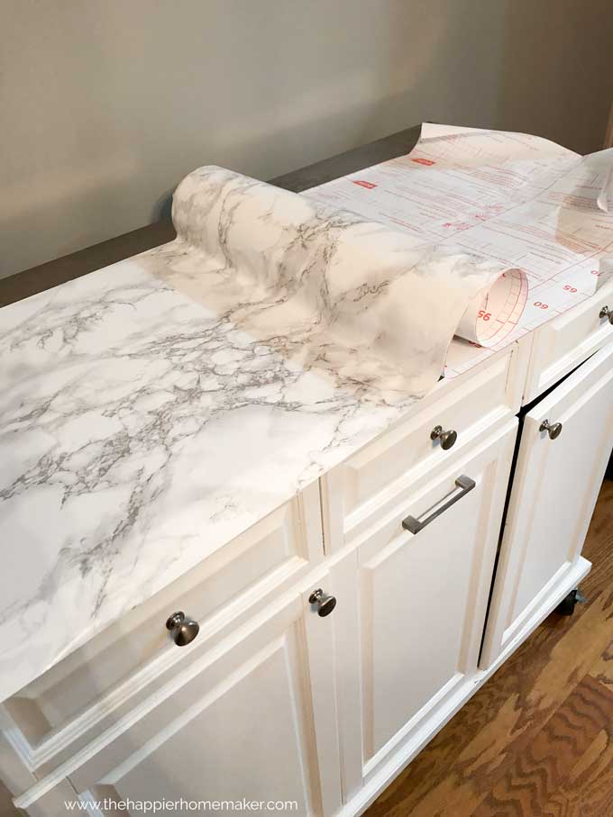 white rolling kitchen island with top being covered in marble contact paper