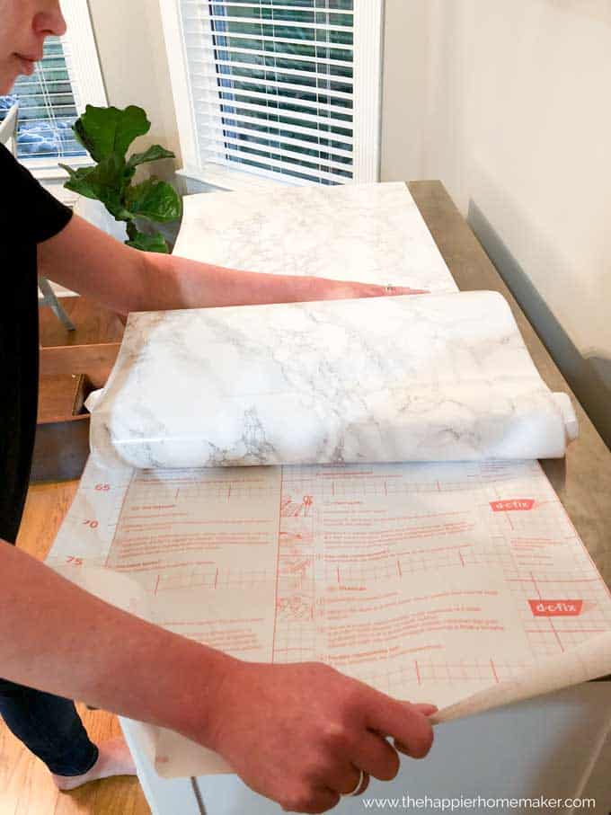 person attaching marble contact paper to top of white rolling kitchen island