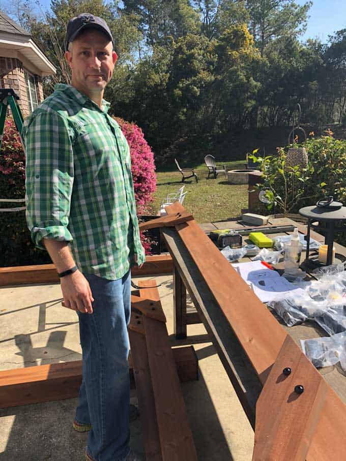 A man standing in front of a picnic table with pergola pieces and tools