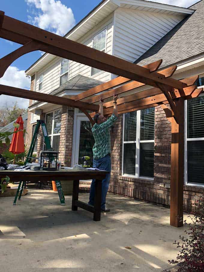 man adding beams to pergola kit being built