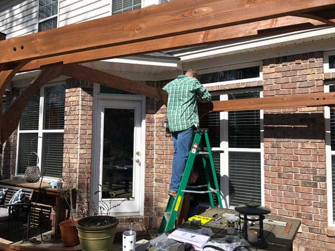 man on ladder adding wood beams to pergola