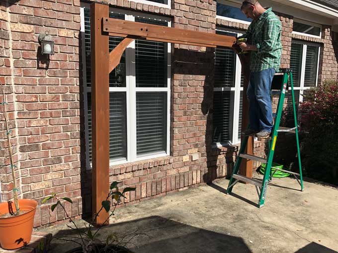 A person standing on a ladder to assemble a pergola kit